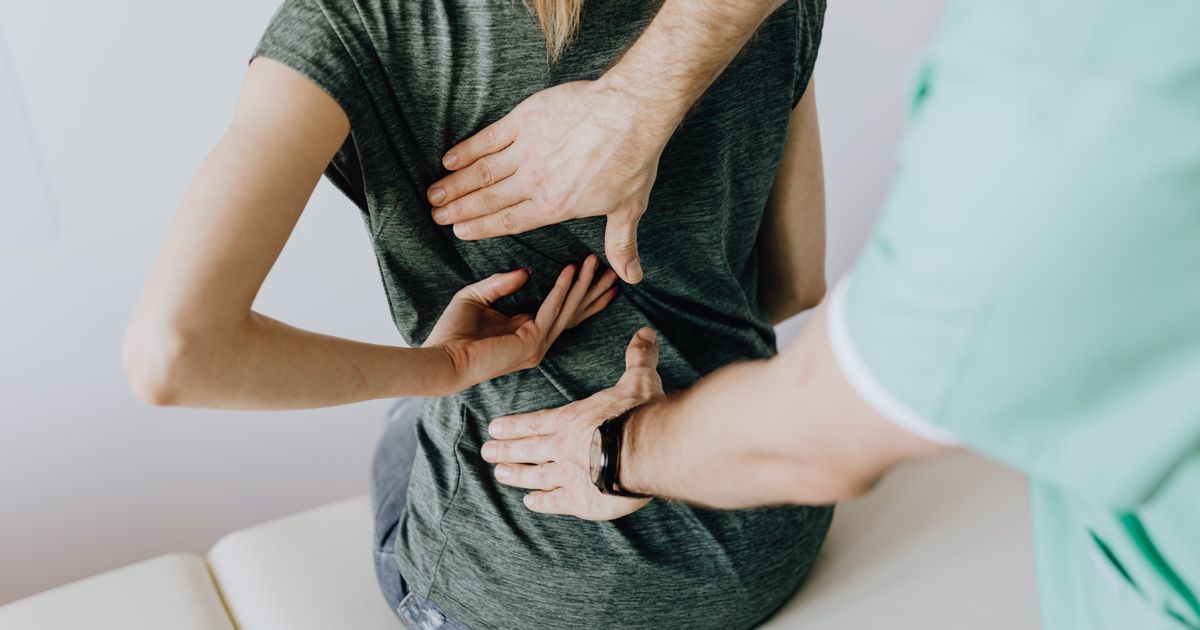 Chiropractor assessing a seated patient's back during an examination