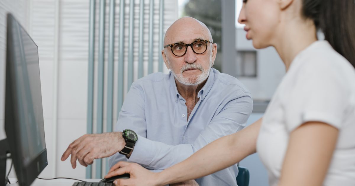 Older man talking with a health care provider at a desk during a consultation