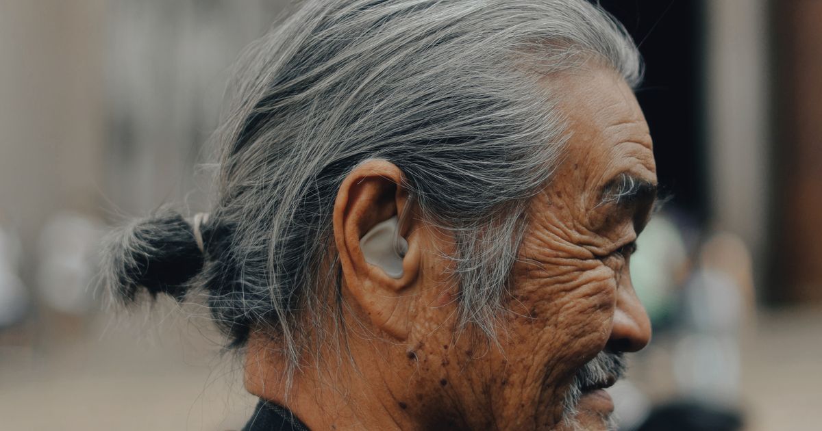 Side profile of a senior man wearing an in-ear hearing aid outdoors