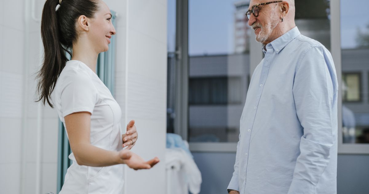 Nurse in a white uniform talking with a senior man in a bright clinic hallway