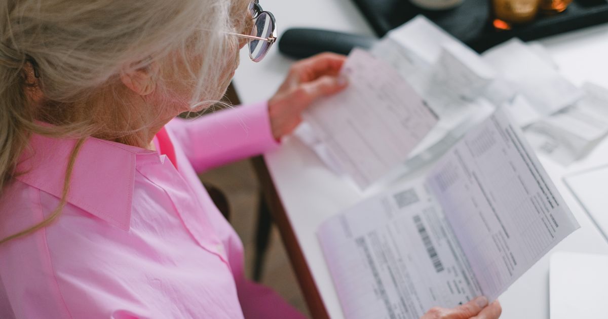 Older woman in glasses calmly reading paperwork at a table at home