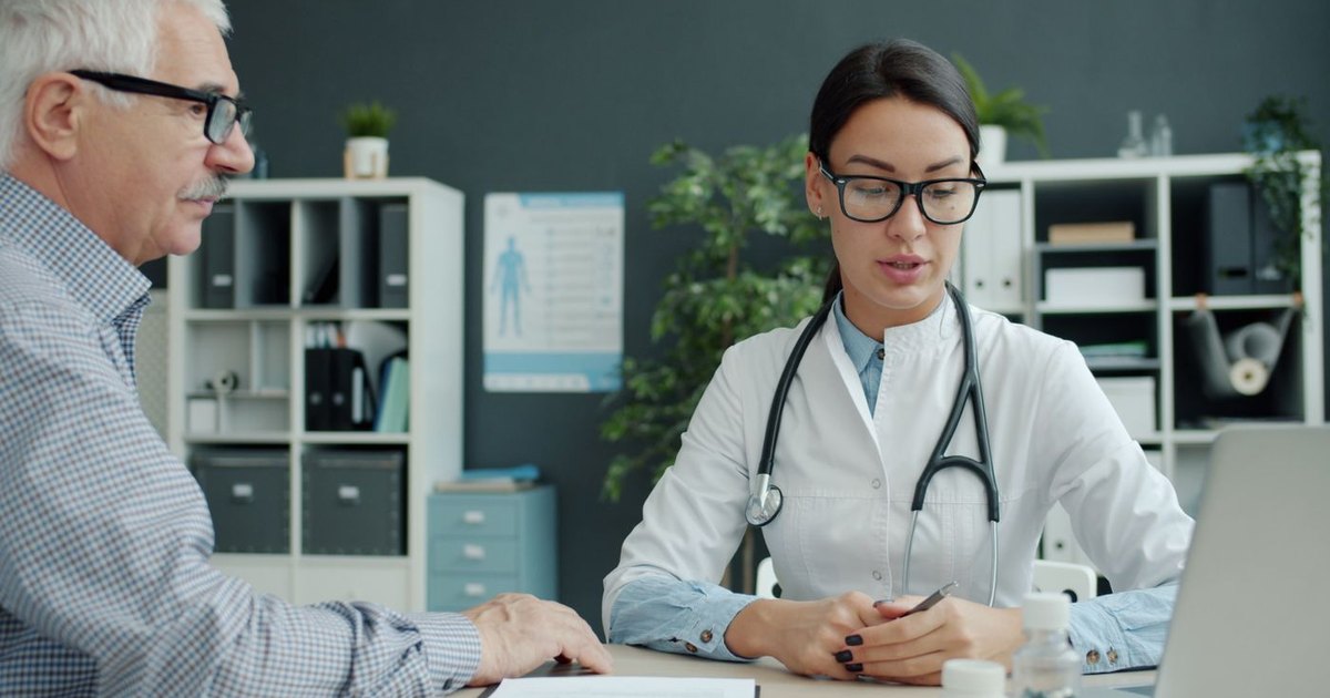 Older man talking with a doctor across a desk in a clinic office