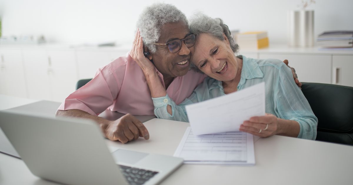 Happy senior couple reviewing a document together at a desk with a laptop